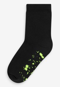 Chaussette noire avec une texture côtelée et un motif éclaboussé en vert fluo en bas. Design de longueur cheville avec un coussin de pied lisse et sans couture.