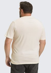 Beige t-shirt met korte mouwen van de achterkant, met een ronde hals en een soepele textuur. Het shirt heeft een relaxte pasvorm zonder zichtbare logo's.