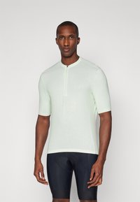 Haut de cyclisme vert clair à manches courtes avec un col haut et une fermeture éclair, associé à un cuissard de cyclisme rembourré noir. Texture lisse.