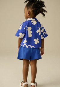 Camicetta blu a maniche corte e pantaloni corti coordinati con motivi astratti bianchi. Tessuto morbido, vestibilità rilassata e design casual adatto per bambini.