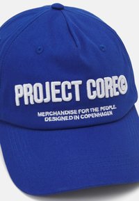 Gorra de béisbol de algodón azul con texto bordado: "PROYECTO CORE" en la parte delantera y "MERCHANDISE PARA EL PUEBLO. DISEÑADO EN COPENHAGUE."
