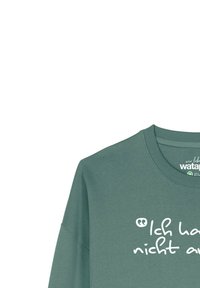 Sweatshirt en coton vert avec un col rond et des manches longues, orné d'un design textuel imprimé en blanc sur le devant.