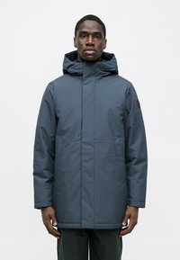 Ναυτικό μπουφάν με κουκούλα φτιαγμένο από λείο, αδιάβροχο ύφασμα. Διαθέτει πλαϊνές τσέπες και ίσια γραμμή, με μια διακριτική λογότυπη λεπτομέρεια στο μανίκι.