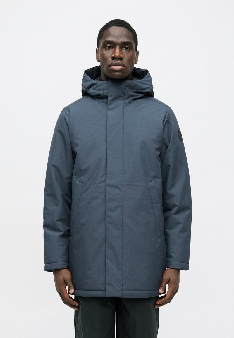 Ναυτικό μπουφάν με κουκούλ�α φτιαγμένο από λείο, αδιάβροχο ύφασμα. Διαθέτει πλαϊνές τσέπες και ίσια γραμμή, με μια διακριτική λογότυπη λεπτομέρεια στο μανίκι.