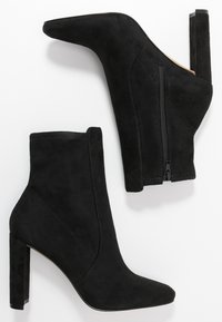 Bottines en daim noir avec un bout pointu, une fermeture éclair latérale et un talon bloc haut. Texture lisse avec des détails de coutures minimales.