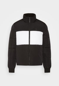 Chaqueta de plumas en blanco y negro con una franja blanca horizontal en el pecho, cremallera frontal, cuello alto y puños acanalados.