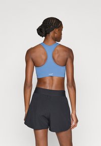 Μπλε αθλητικό σουτιέν με σχέδιο racerback, συνδυασμένο με μαύρο, άνετο σορτς. Διαθέτει λογότυπο στην πλάτη του σουτιέν.