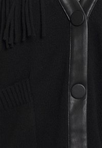 Czarny kardigan z fakturowanym dzianinowym korpusem, skórzanymi wykończeniami i okrągłymi guzikami. Posiada kieszeń oraz ozdobne frędzle.