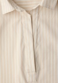 Beżowa koszula z pionowymi białymi paskami, z klasycznym kołnierzykiem, zapięciem na listwę oraz gładką fakturą i starannym szyciem.