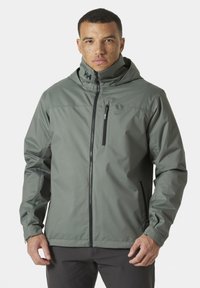 Waterdichte, capuchonjack in gedempt groen. Heeft een voorrits, zijzakken en een logo-detail op de kraag. Gladde textuur.