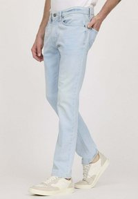 Jean en denim bleu clair avec une coupe slim, cinq poches et un léger délavage. Assortis à des baskets beiges et blanches.