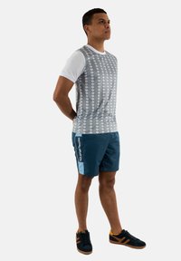 Camisa de manga corta a rayas grises y blancas, combinada con pantalones cortos azules con detalles laterales y logotipo, llevada con zapatos negros.