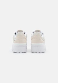 Low-top sneakers featuring a two-tone design with beige suede and white leather, textured accents, and a thick white rubber sole.