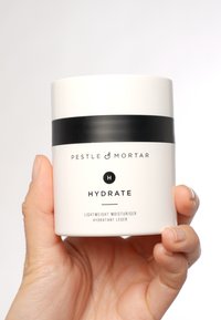 Conteneur cylindrique blanc avec une bande noire, étiqueté "HYDRATE", contenant un hydratant léger. Design épuré et minimaliste.