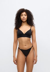 Μαύρο σετ μαγιό μπικίνι που περιλαμβάνει bralette με λεπτές τιράντες και μαγιό με χαμηλή μέση. Το ύφασμα είναι λείο με ελάχιστες ραφές και διακοσμητικές λεπτομέρειες.