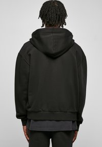 Sweatshirt à capuche noir avec une texture douce, coupe décontractée, épaules tombantes et ourlet côtelé. La vue arrière montre un design sans couture et la profondeur du tissu.