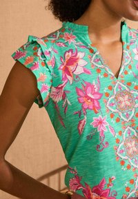 Green floral top with ruffled sleeves, featuring pink and orange flowers, a v-neckline, and intricate patterns. Soft fabric texture.