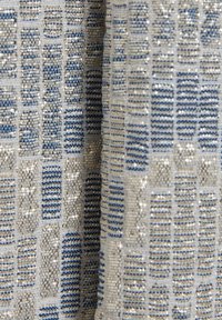 Gros plan sur un tissu texturé avec des motifs tissés rectangulaires verticaux bleu et beige et des fils subtilement chatoyants.