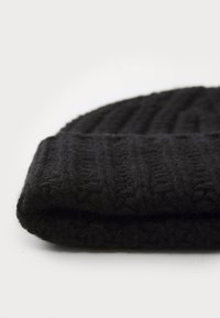 Crna pletena zimska kapa s reljefnim rebrastim uzorkom, izrađena od vune, sa sklopivim rubom na dnu, koja prikazuje meku završnu obradu.