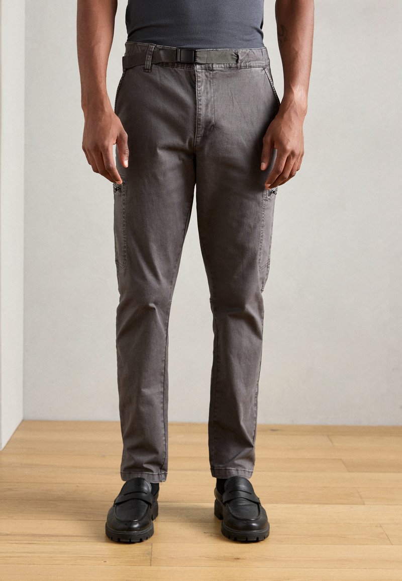 Sivé slim-fit nohavice s pútkami na opasok, bočnými zipsami a prednými vreckami. Vyrobené z odolného materiálu, s hladkou textúrou a minimálnym prešitím.