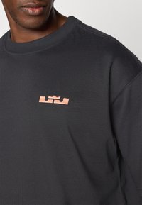Czarny sweatshirt z okrągłym dekoltem wykonany z mieszanki bawełny. Posiada haftowane logo w kolorze miedzi na lewej piersi. Teksturowany materiał.