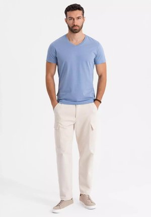 Camiseta de pico en azul claro combinada con pantalones cargo color crema. Tejido texturizado y bolsillos laterales, complementados con zapatillas beige.
