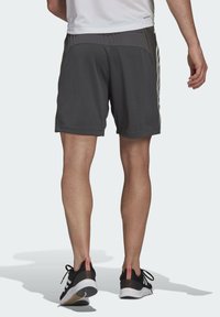 Pantalones cortos deportivos grises con una textura suave, que presentan una cinturilla oscura en contraste y tres rayas verticales blancas en cada lado.