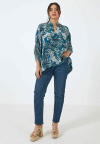 Blue and gray patterned blouse with a high neck, loose fit, and flowing sleeves, paired with denim jeans and chunky platform sandals.