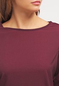 Burgunderfarbener Stretch-Top mit weit ausgeschnittenem Halsausschnitt und glatter Textur, ausgestattet mit kurzen Ärmeln und einer taillierten Silhouette.