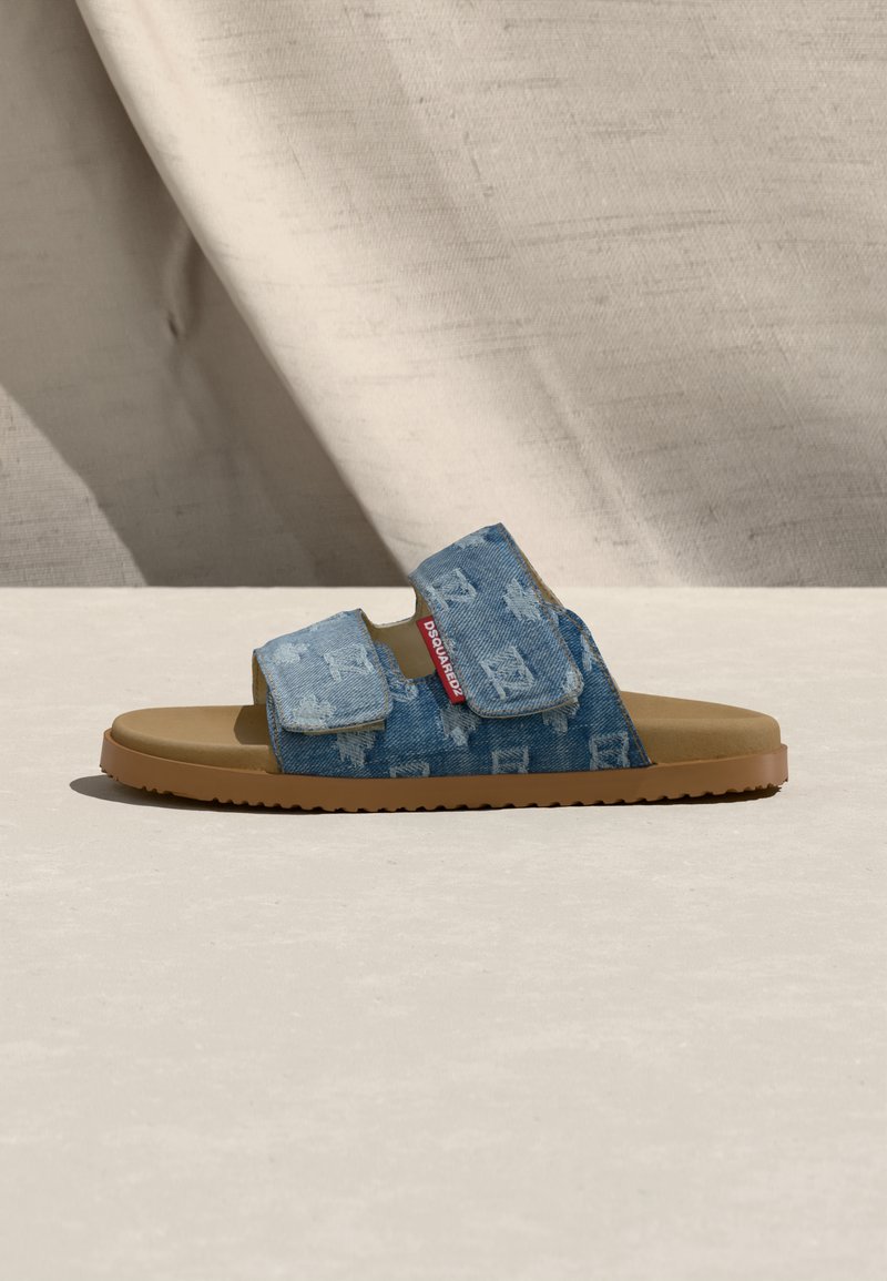 Sandale à glissière avec semelle beige et deux brides réglables en denim bleu présentant un motif subtil et une étiquette de marque rouge sur le côt é.