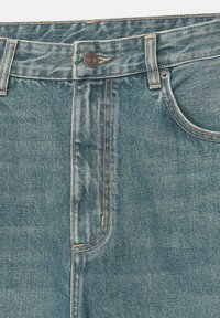 Svijetloplave traperice ravnog kroja, s patent zatvaračem, prednjim džepom i vidljivim šavovima.