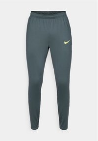 Tamno sive tajice za sport s elastičnom strukom i istaknutim žutim Nike logotipom na gornjoj lijevoj butini. Glatka, lagana tkanina.
