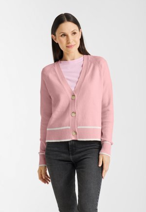 Lichtroze cardigan gemaakt van zachte stof, met een knoopsluiting aan de voorkant, ribbelboorden en een zoom met witte streepaccenten. Draag het over een roze top.
