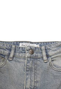 Helle blaue Denim-Jeans mit einem verwaschenen Look, ausgestattet mit einem Knopfverschluss mit "B&R"-Logo und einem Etikett am Bund.
