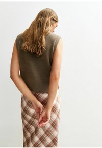 Ärmelloses, braunes Strickoberteil, kombiniert mit einem karierten Rock in Beige, Braun und Orange. Glatte Textur mit taillierter Form und dezenten Design-Details.