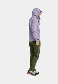 Light purple hooded jacket with a fitted design, paired with dark green pants featuring zippered pockets and gray athletic shoes.