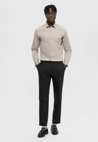 Ljusbeige skjorta med knappar och långa ärmar, kombinerad med svarta skräddarsydda byxor och svarta loafers med guldaccent.