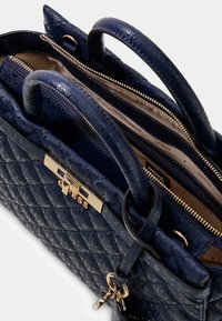 Granatowa pikowana torebka na ramię z zapięciem w kolorze złotym i podwójnymi uchwytami. Wnętrze posiada wiele przegródek wykończonych satynowym materiałem.