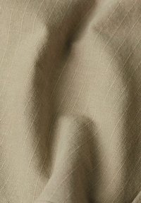 Tessuto beige con un motivo testurizzato a righe, caratterizzato da morbide pieghe e una superficie liscia, che indica un materiale leggero.