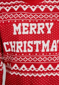 Rode gebreide trui met grote witte tekst "MERRY CHRISTMAS," met geometrische patronen en decoratieve elementen in contrasterend wit.