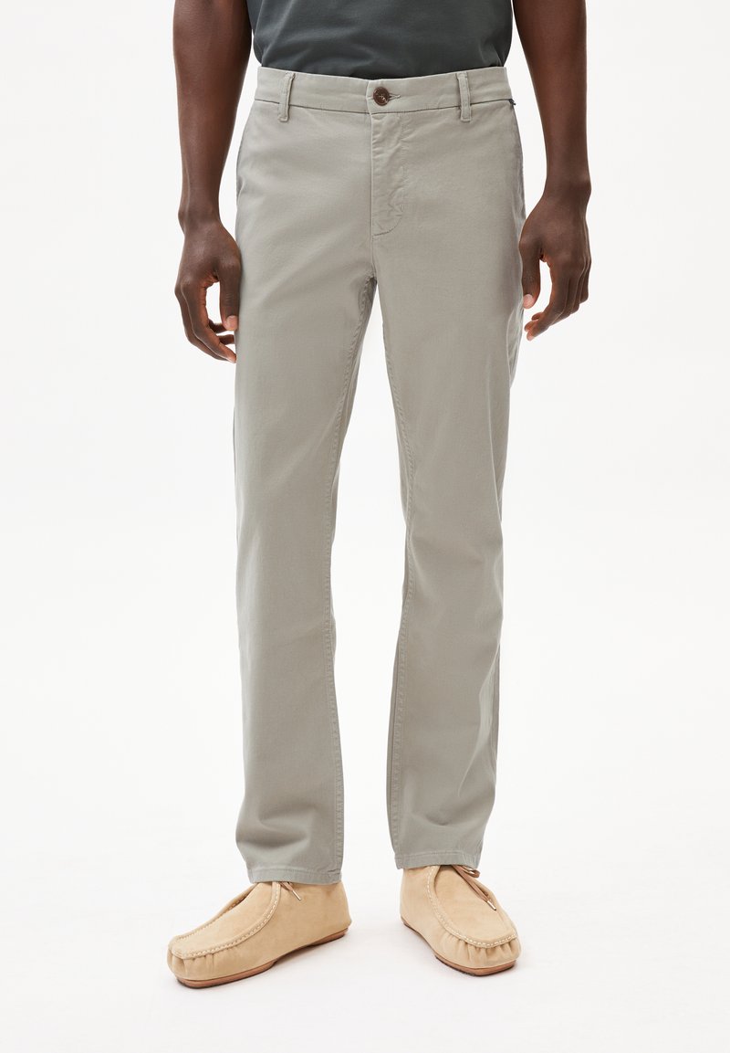 Pantaloni grigi chiari in cotone con una vestibilità slim, dotati di chiusura con bottone e tasche laterali. Abbinati a pantofole morbide color beige.