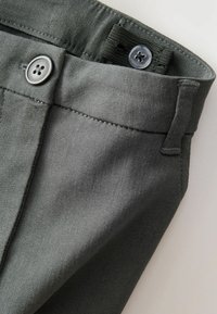 Pantaloni in cotone grigi con una texture liscia, due bottoni in vita e cuciture sartoriali lungo le cuciture.