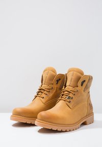 Botas de tobillo de cuero marrón con suela resistente, que cuentan con ojales de metal, un cuello acolchado y marca lateral. Acabado liso y texturizado.
