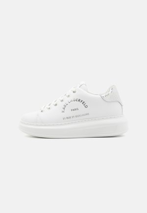 Witte sneaker met een leren bovenwerk, zilveren glinsteraccenten op de hiel en gegraveerde merkdetailles. Kenmerkt zich door ronde veters en een dikke zool.