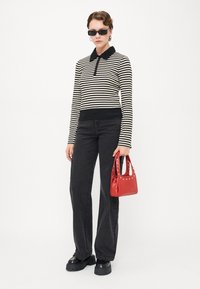 Stripet langermet polo-skjorte i svart og hvitt, kombinert med høytaljede svarte jeans. Tilbehøret inkluderer en liten rød veske med nagler og svarte plattformsko.