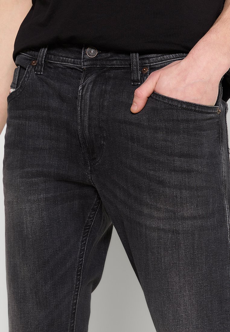 Dunkelgraue Denim-Jeans verfügen über einen klassischen Schnitt mit einer strukturierten Oberfläche, fünf Taschen und einem Knopfverschluss, der detaillierte Nähte und subtile Verfärbungen zeigt.