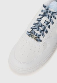 White sneaker with textured leather upper, navy and white patterned laces, perforated toe box, and metallic tag labeled "AF1."