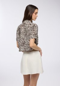 Camicetta a maniche corte a motivo zebra marrone e bianco abbinata a una gonna bianca leggera e con texture. La camicetta ha una vestibilità rilassata e collo.