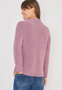 Fioletowy sweter wykonany z miękkiego, puszystego materiału. Posiada długie rękawy, okrągły dekolt i luźny krój, stylizowany z niebieskimi dżinsami.
