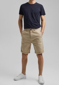Granatowa koszulka z okrągłym dekoltem w połączeniu z khaki spodniami typu rolled shorts. Spodnie mają zapięcie na guzik i kieszenie po bokach. Białe sneakersy dopełniają strój.